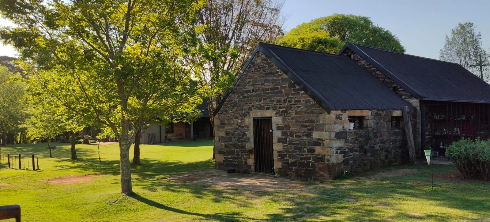 A stone farm building beneath mature trees in afternoon light.